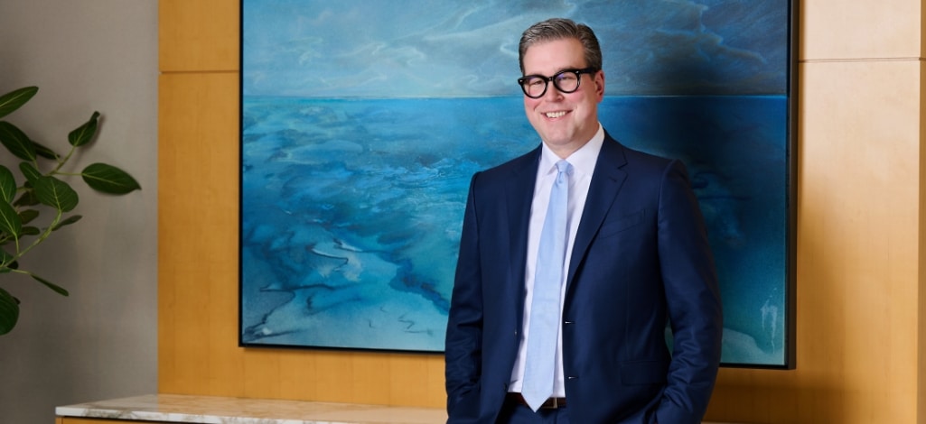 Managing Partner in a blue suit leans against table in corporate setting